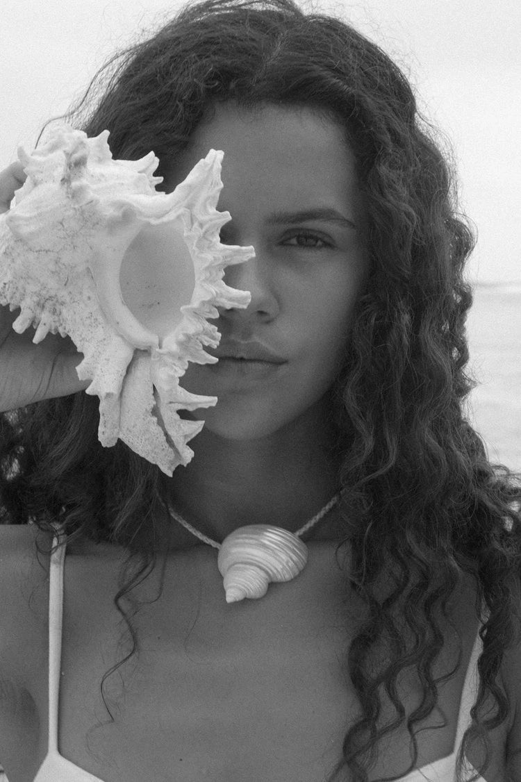 Black and white photo of a woman holding a large shell to her face with another shell necklace.
