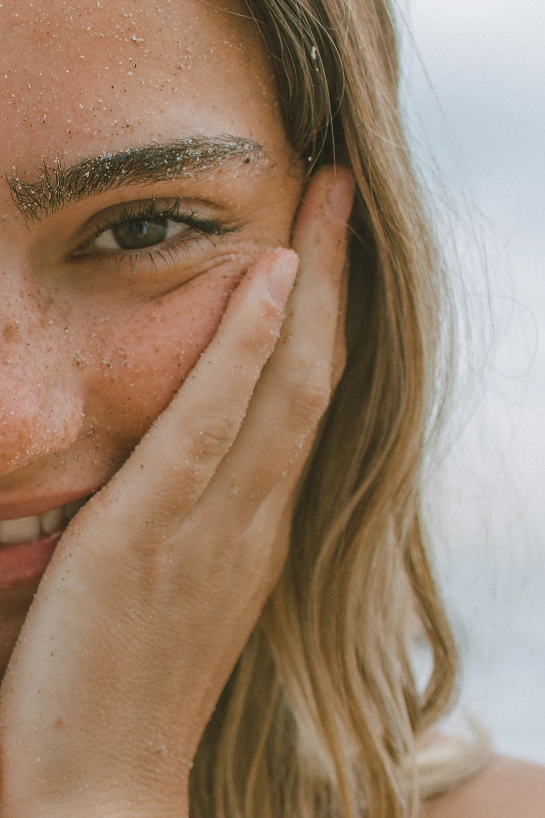 Close-up of a person with blonde hair and freckles, holding their hand near their face.