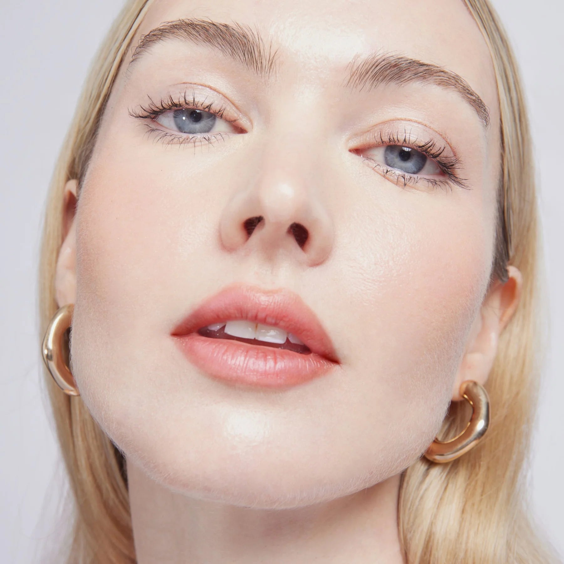 Close-up of a woman's face with blonde hair and gold hoop earrings on a light background