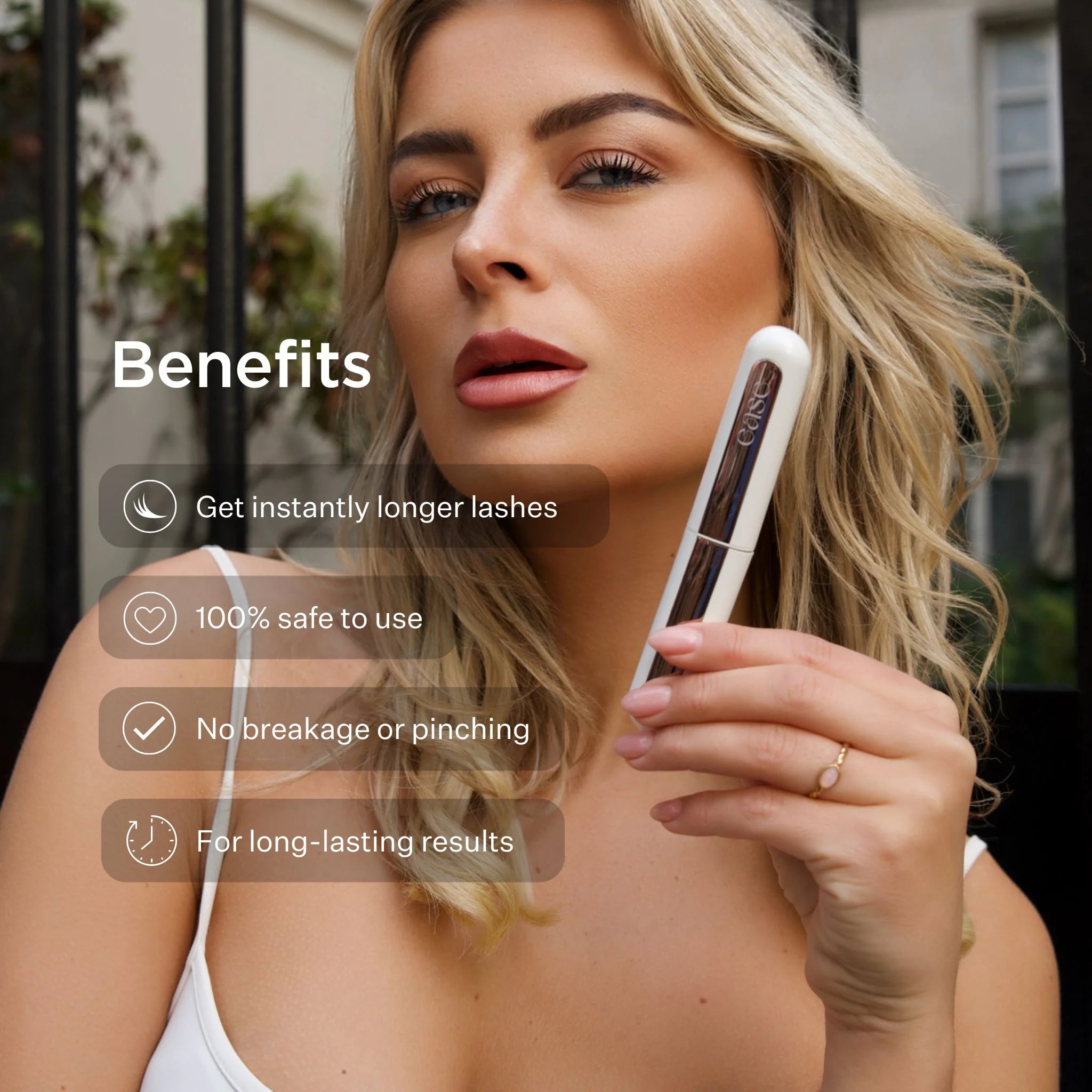 Woman holding a heated lash curler with benefits listed on a blurred outdoor background
